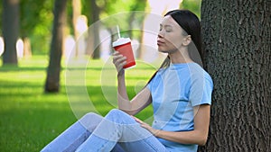 Careless asian woman throwing away empty paper glass siting under tree in park