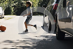 Careless boy running behind the ball on the road next to cars