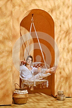 Careless senior woman sits on swing in shade hiding from the heat of the sun