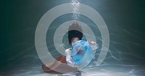 Careless waste disposal. Young mixed race woman diving, floating under water to throw out blue garbage bag slow motion.