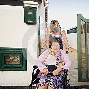 The carer drives the old lady out of the house in a wheelchair