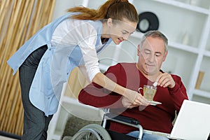 Carer giving drink to man in wheelchair