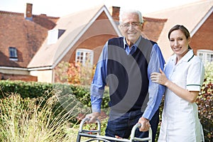 Carer Helping Senior Man To Walk In Garden Using Walking Frame