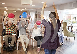 Carer Leading Group Of Seniors In Fitness Class In Retirement Home