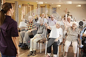 Carer Leading Group Of Seniors In Fitness Class In Retirement Home