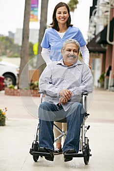 Carer Pushing Disabled Senior Man In Wheelchair