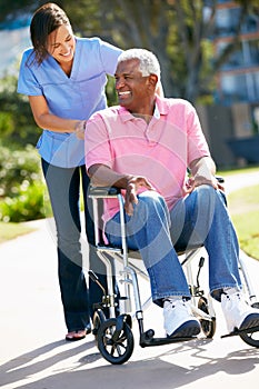 Carer Pushing Senior Man In Wheelchair