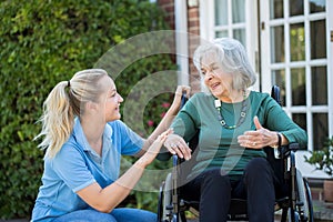 Carer Pushing Senior Woman In Wheelchair Outside Home