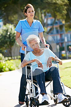 Carer Pushing Unhappy Senior Woman In Wheelchair