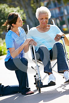 Carer Pushing Unhappy Senior Woman In Wheelchair