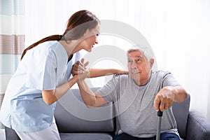 Caretaker Assisting Senior Man To Get Up From Sofa photo