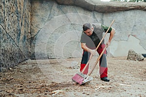 Caretaker with down syndrome in zoo cleaning animal enclosure. Concept of integration people with disabilities into