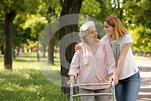 Caretaker helping elderly woman with walking frame