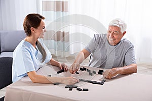 Caretaker Looking At Elder Man Playing Dominoes photo