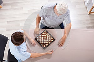 Caretaker Playing Chess With Senior Man On Desk photo