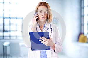 Careworn female doctor using mobile phone while standing in exam room