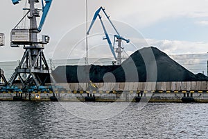 Cargo cranes in the port coal terminal. Pile of coal on the pier