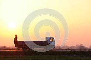 Cargo dump truck driving on highway hauling goods in evening. Delivery transportation and logistics concept