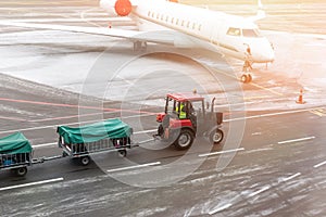 cargo freight tractor machine delivering luggage carts to airplane at airport. Airport carrier and service