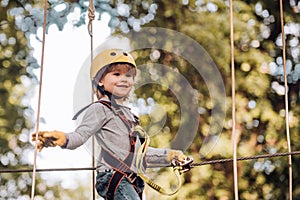 Cargo net climbing and hanging log. Cute school child boy enjoying a sunny day in a climbing adventure activity park