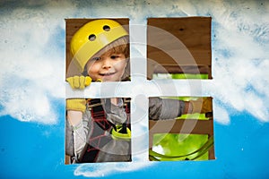 Cargo net climbing and hanging log. Helmet and safety equipment. Child boy having fun at adventure park. Carefree