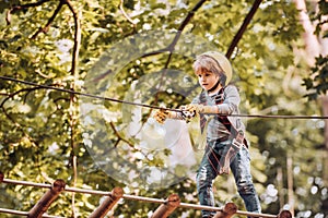 Cargo net climbing and hanging log. Hiking in the rope park girl in safety equipment. Happy child climbing in the trees