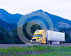 Cargo semi truck reefer trailer yellow on green highway winding