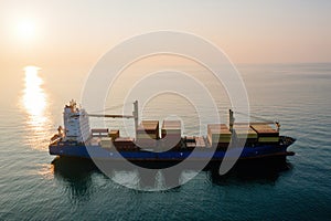 Cargo ship with containers in the open sea at the sunset, aerial drone view
