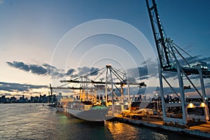 Cargo ship and cranes in sea port on evening sky. Maritime container port or terminal. Shipping freight and merchandise