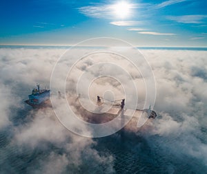 Cargo ship and cranes silhouettes in sea fog, crane vessel working for delivery of delivery containers