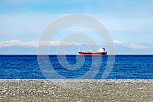 Cargo ship in open sea against the background of snow covered mountains.