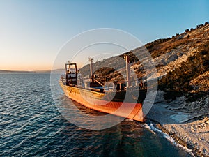 Cargo ship run aground at sea coastline. Shipwreck accident of nautical vessel after huge sea storm, aerial view