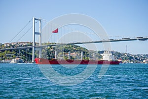 A cargo ship sails under a bridge in Istanbul on a summer and sunny day