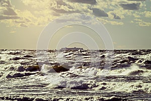 Cargo ship silhouette on the horizon. Large container vessel sailing through stormy waves of the Baltic Sea.