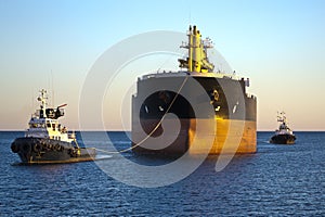 Cargo ship with two tug boats assistance
