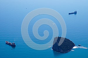 The cargo ships are at anchor near Antalya (Turkey) bay with the rocky island - aerial drone view