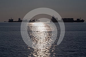 Cargo Ships full of containers lining in front of Thessaloniki port at Sunset into the light.
