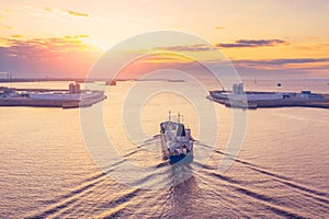 Cargo tanker with oil products sails in the harbor of an industrial city port at dawn in the morning, aerial view