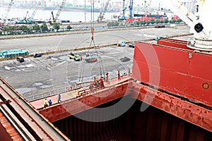 Cargo terminal for unloading steel plates from bulk carrier by ships cranes. View of the pier, cranes and various equipment. Port