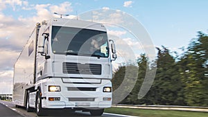 Cargo truck with cargo trailer driving on a highway. White Truck delivers goods in early hours of the Morning - very low angle