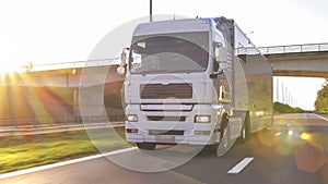 Cargo truck with cargo trailer driving on a highway. White Truck delivers goods in early hours of the Morning - very low angle