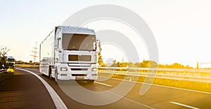 Cargo truck with cargo trailer driving on a highway. White Truck delivers goods in early hours of the Morning - very low angle