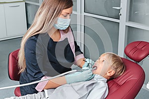 Caries treatment procedure in stomatology clinic close-up. Dentist in uniform holding dental tools. Young boy sitting in the chair