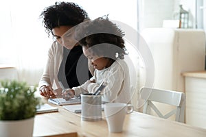 Caring African American mother helping to little daughter with homework