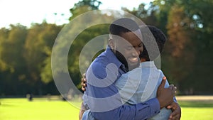 Caring afro-american dad embracing teen son in park, family relationships, love