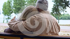 Caring aged husband covering wife with plaid blanket and hugging, tenderness