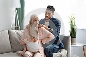 Caring arab husband making neck massage to pregnant muslim wife at home photo