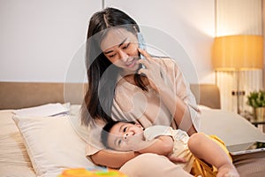 A caring Asian mom is putting her little son to sleep in her arms while she is talking on the phone