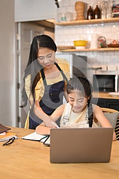 Caring asian mother helping daughter doing homework in kitchen table
