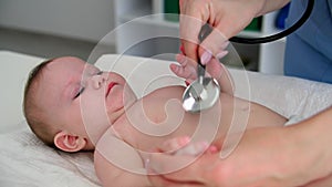 caring for baby, a female doctor using a phonendoscope listens to breathing of a small child on a pelination table in